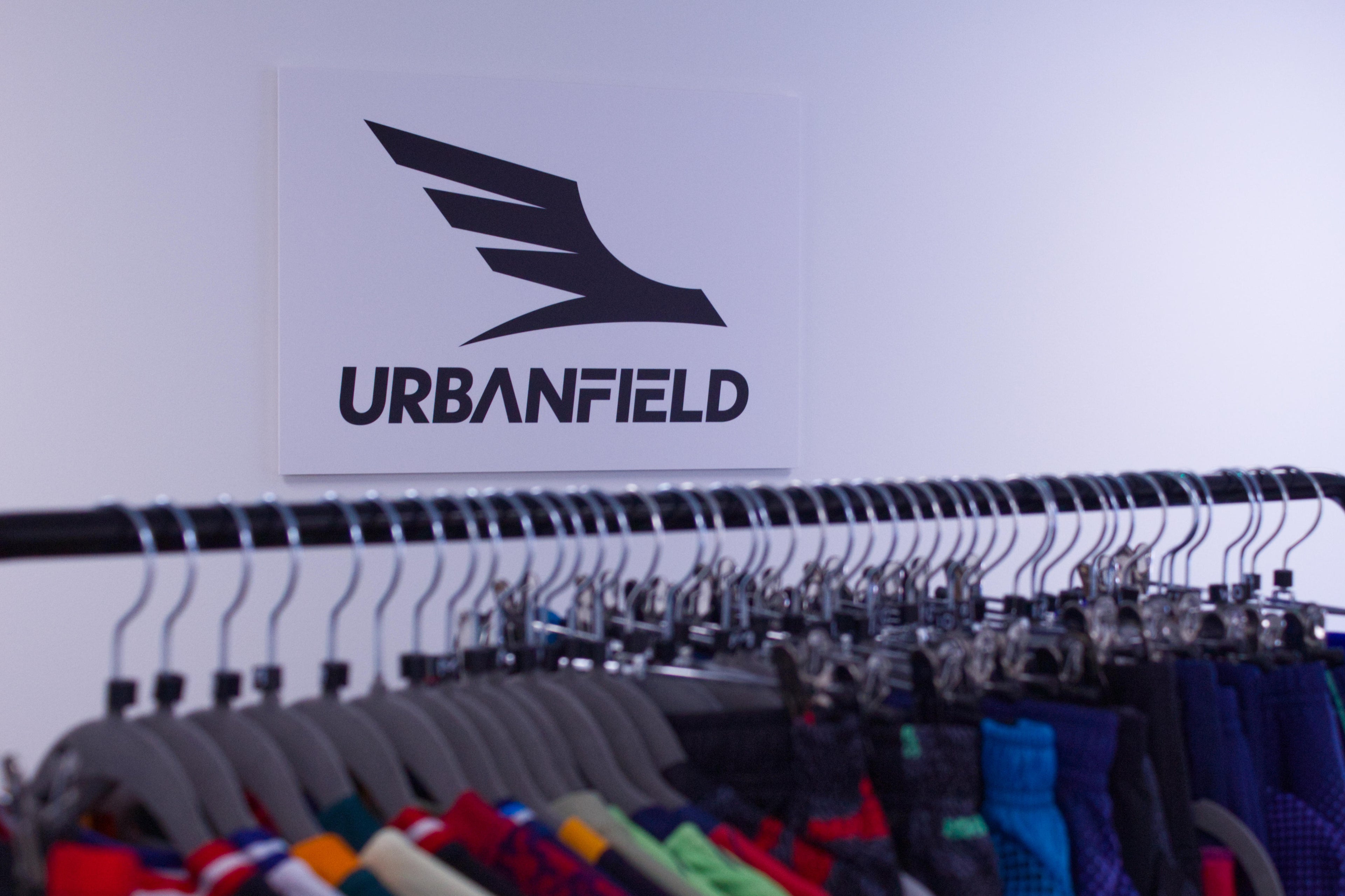Urbanfield Sports logo on a white wall with hangers and sports clothes in the foreground.