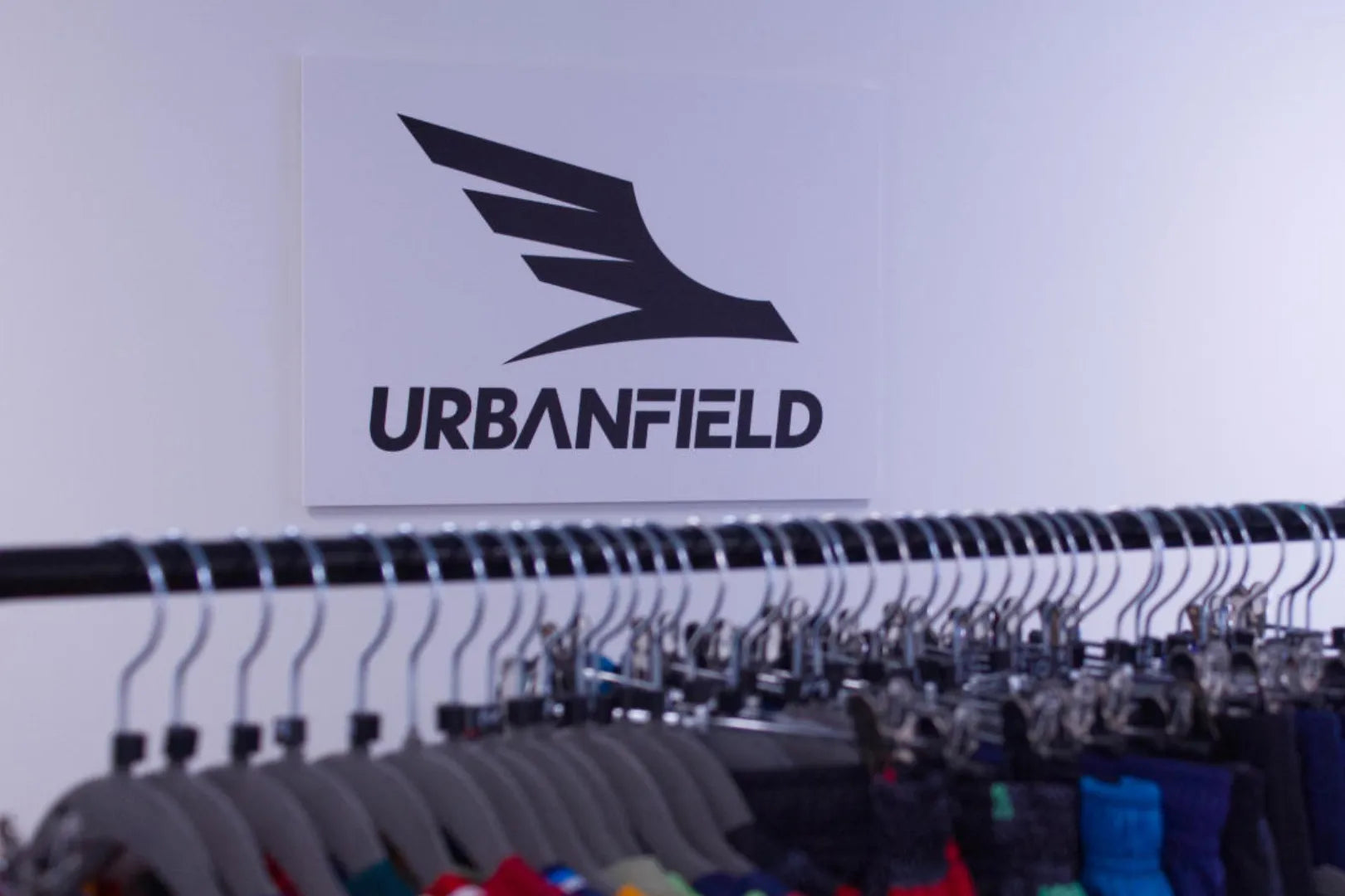 Urbanfield Sports logo on a white wall with hangers and sports clothes in the foreground.