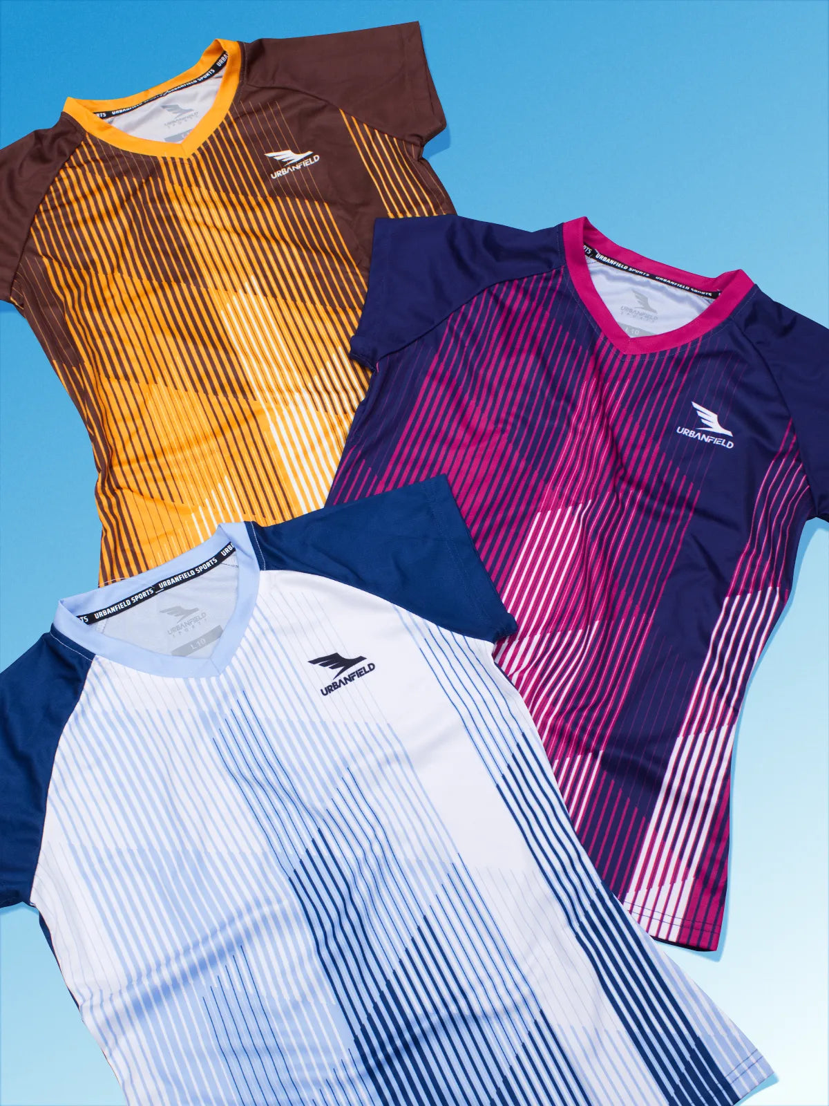 Three women's Urbanfield Sports Ignis t-shirts, in slate blue, navy and brown on a light blue background.