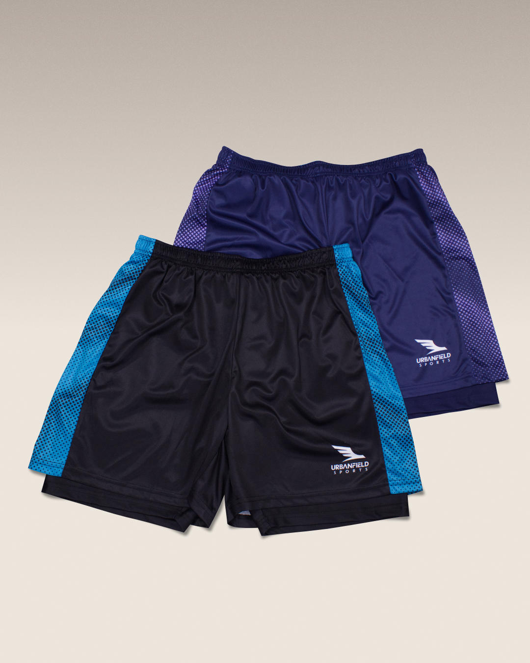 Two pairs of Urbanfield Sports shorts, one black with turquoise accents and one navy blue with lilac accents, on a beige background.