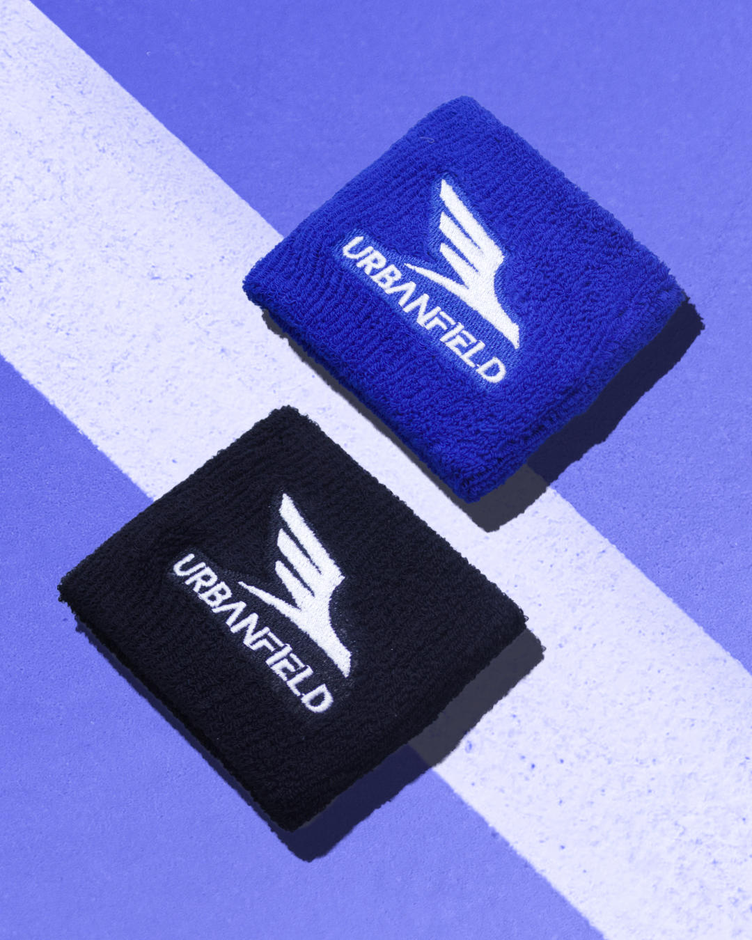 Two wristbands, one blue and one black, with Urbanfield Sports logo on a blue and white striped background.