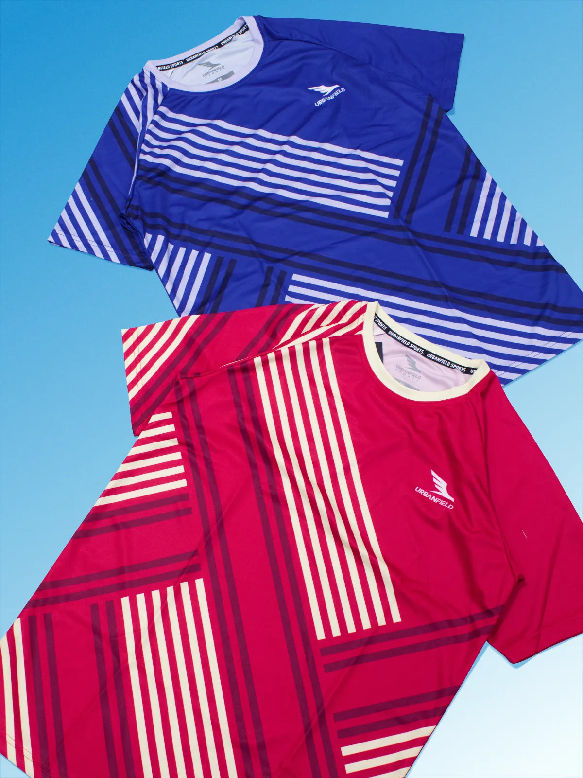 Two Men's Urbanfield Sports Serve t-shirts, one in cherry red and the other in royal blue on a light blue background.