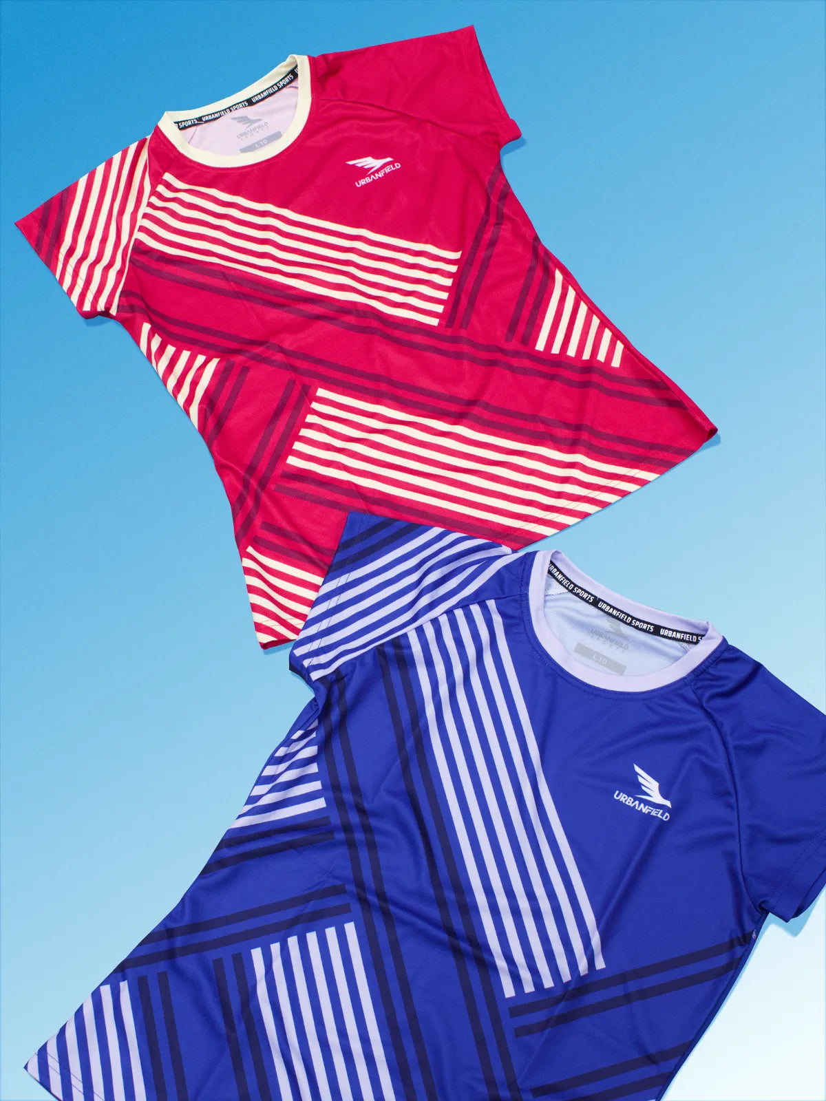 Two Women's Urbanfield Sports Serve t-shirts, one in cherry red and the other in royal blue on a light blue background.