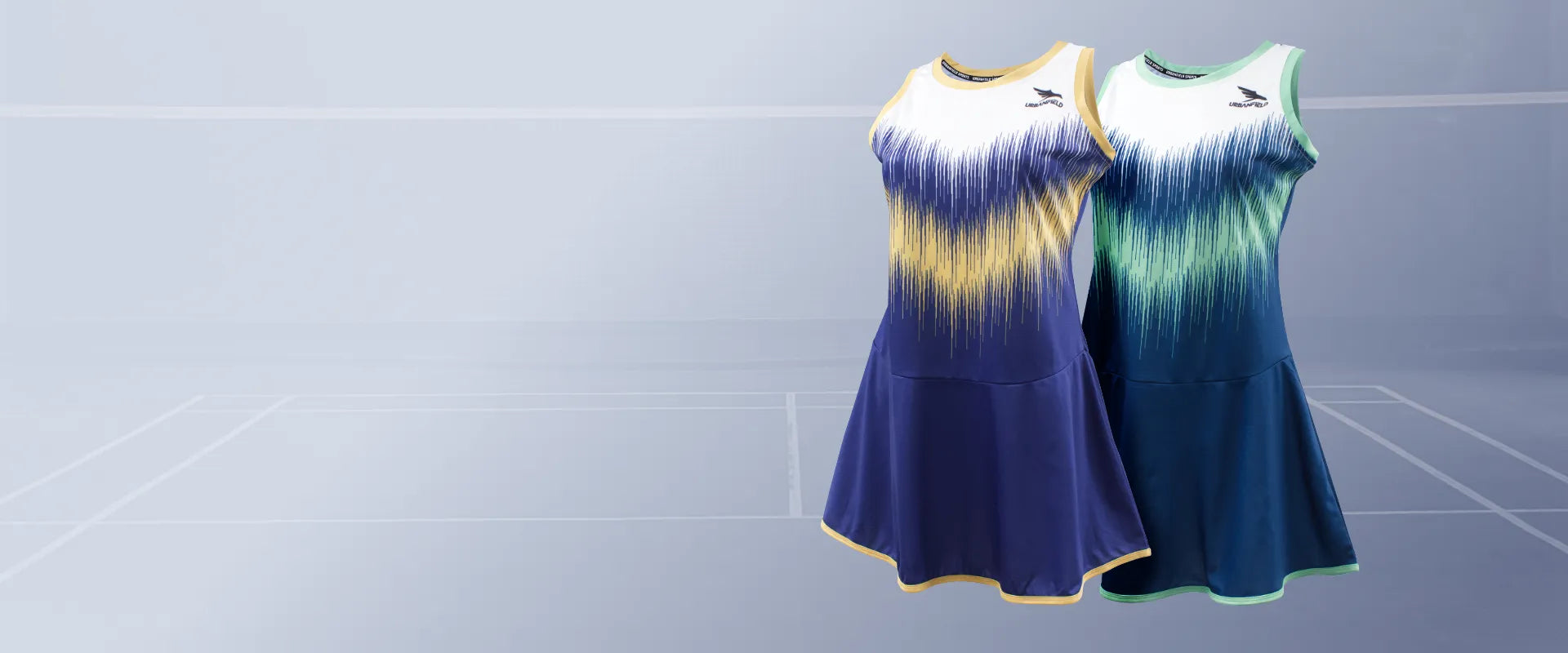 Two Urbanfield Sports women's striker sleeveless dresses, one in carbon navy and the other in slate blue, are displayed against a grey badminton court background.