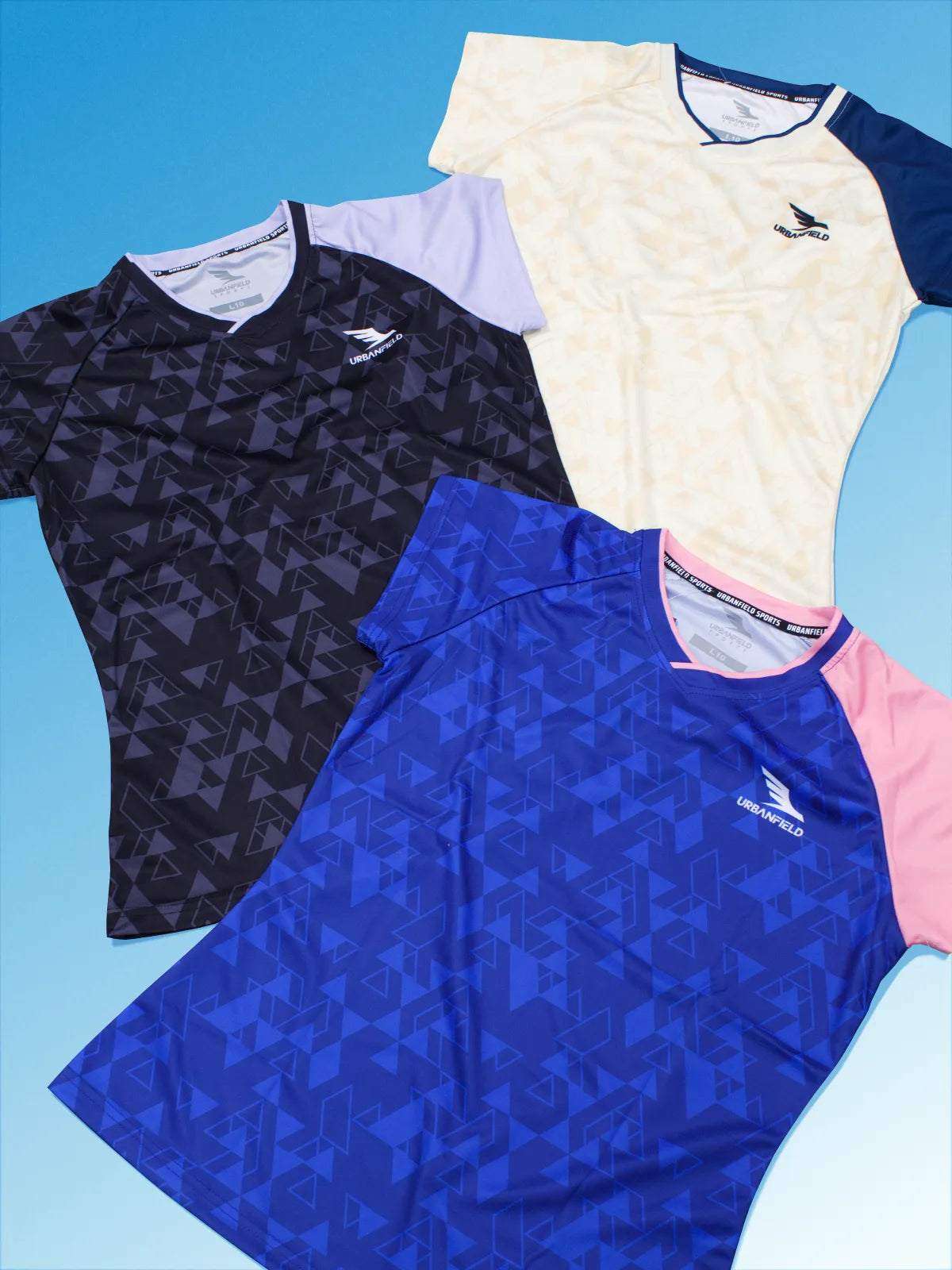 Three women's Urbanfield Sports Trianguli t-shirts, in royal blue, black and sand on a light blue background.
