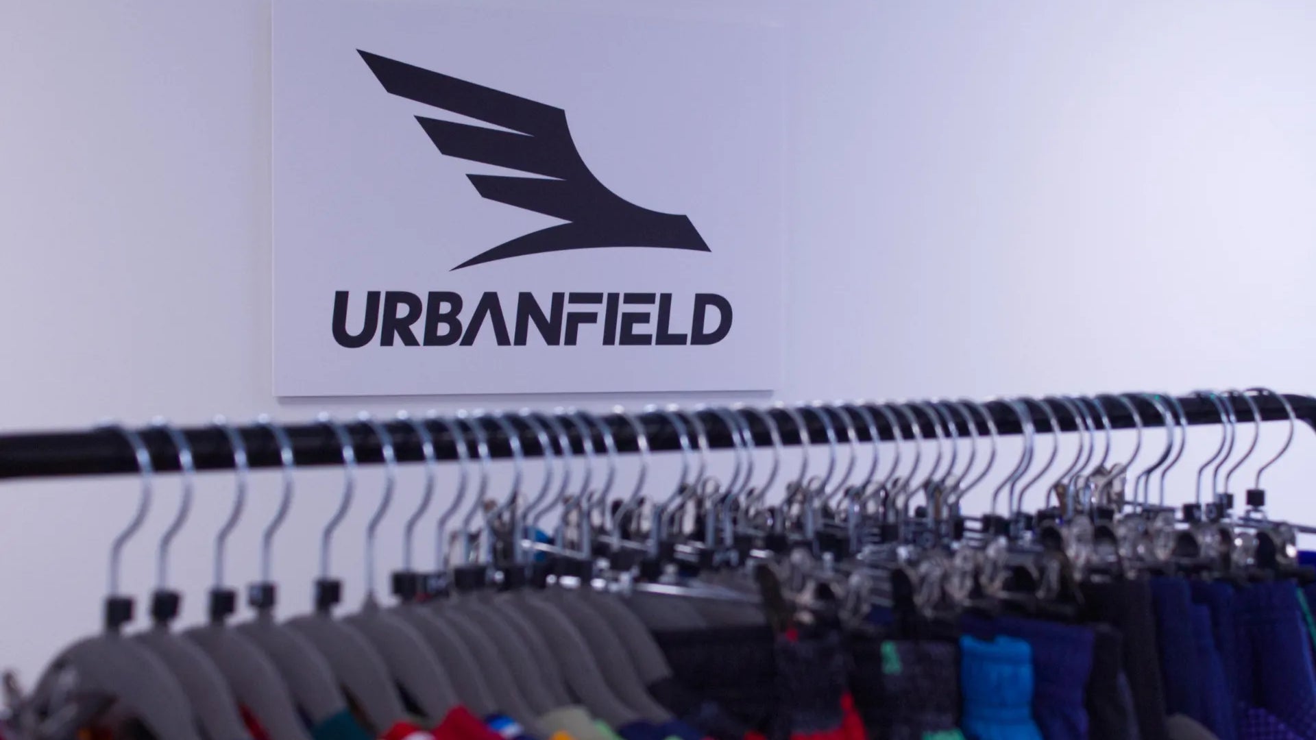 Urbanfield Sports logo on a white wall with hangers and sports clothes in the foreground.