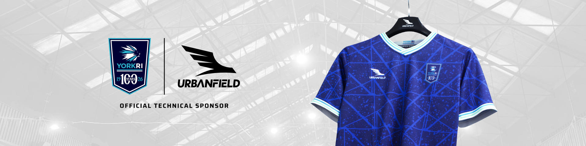 York RI Centenary shirt on a black Urbanfield Sports hanger in front of a white background featuring the York RI roof.